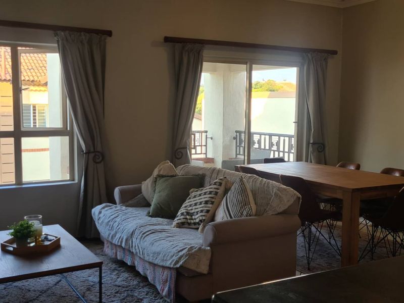Open plan living and dining area featuring large windows, sliding doors to a balcony, and neutral tiled flooring.