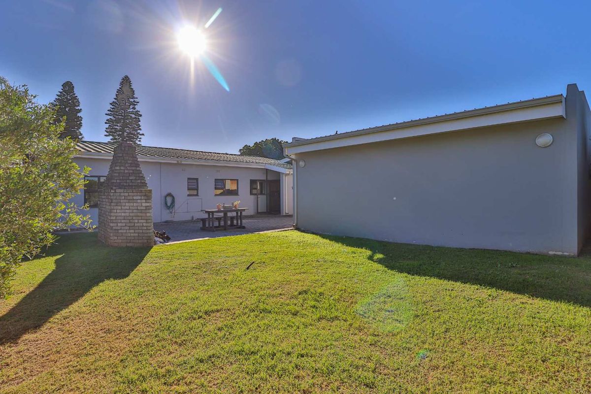 A rear garden area featuring a paved patio, a built-in brick fireplace, and a lawn space adjacent to the house exterior.