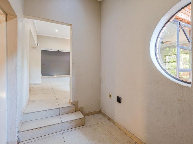 A bright, empty hallway featuring tiled flooring, a distinctive circular window, and a stepped transition leading into an adjacent living space.