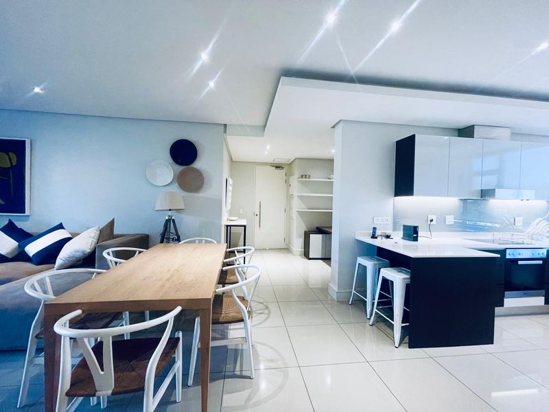 Modern open-plan living and dining area featuring a sleek kitchen with stone countertops, integrated appliances, and polished tiled flooring throughout.