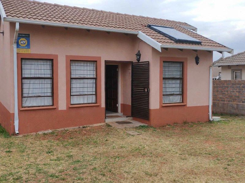 Front view of a single-story house featuring a tiled roof with a solar water heater, security gate, and surrounding brick boundary walls.