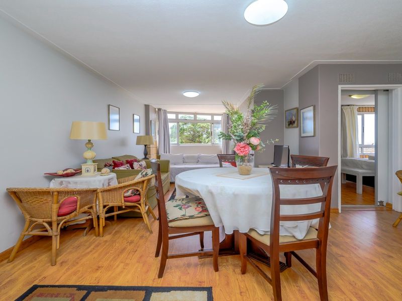 An open-plan living and dining area featuring laminate flooring and neutral wall tones, providing a functional layout with access to an adjacent room.