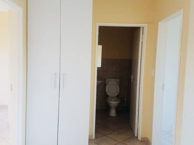 A clean hallway featuring neutral wall tones, tiled flooring, and a built-in storage cupboard, providing access to adjacent rooms.