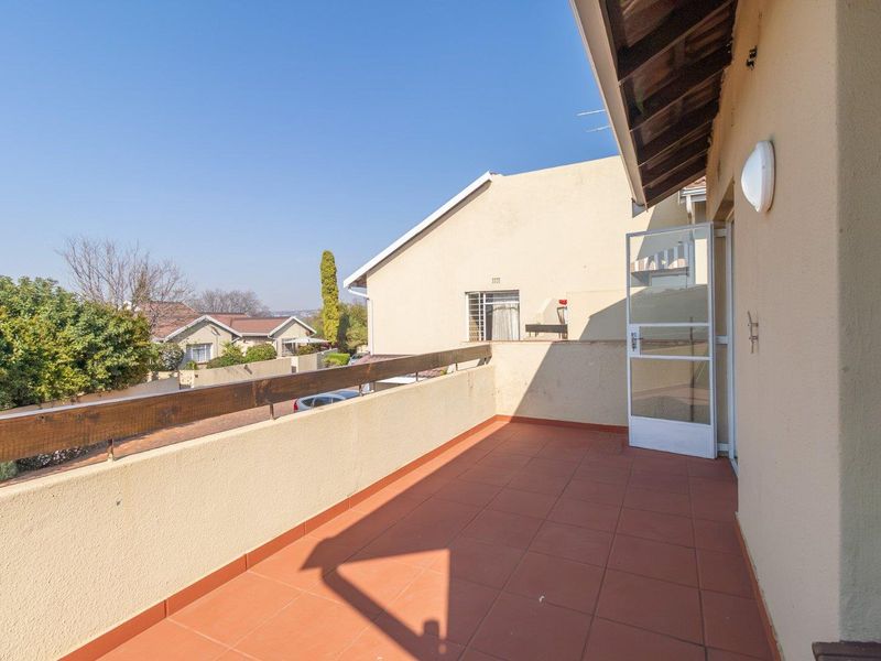 An open-air balcony featuring terracotta-style tiled flooring, a timber balustrade, and direct access to the interior through a glass panel door.