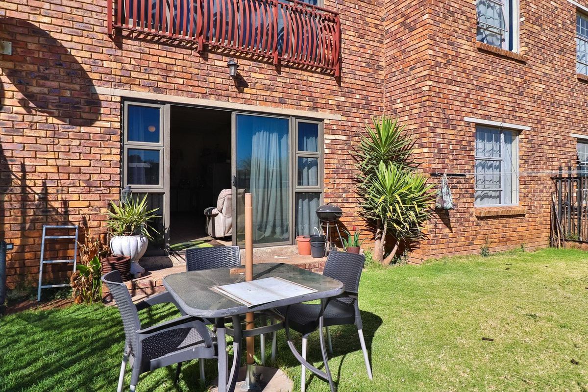 Rear view of the apartment featuring a private garden area, brick facade, and sliding glass doors leading into the living space.