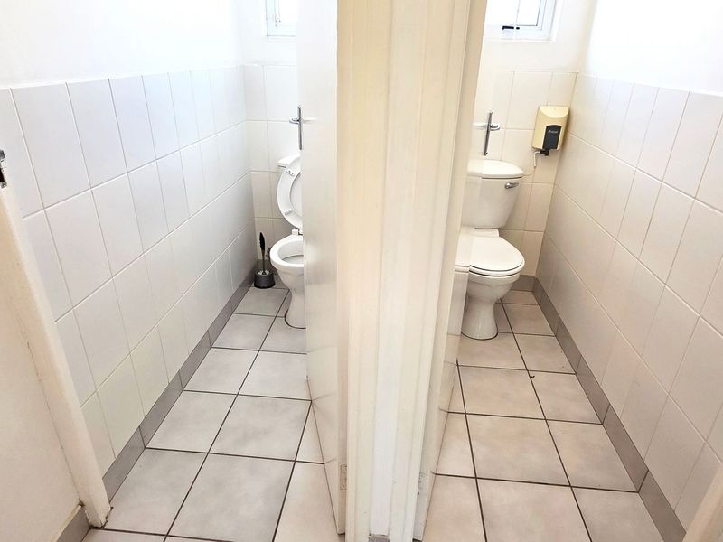 A functional office restroom facility featuring two separate toilet cubicles with tiled walls and floors.
