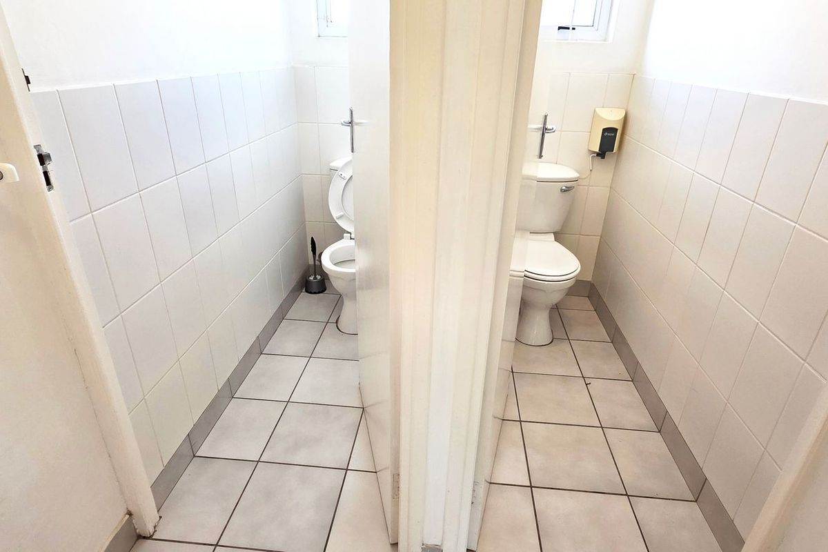 A functional office restroom facility featuring two separate toilet cubicles with tiled walls and floors.
