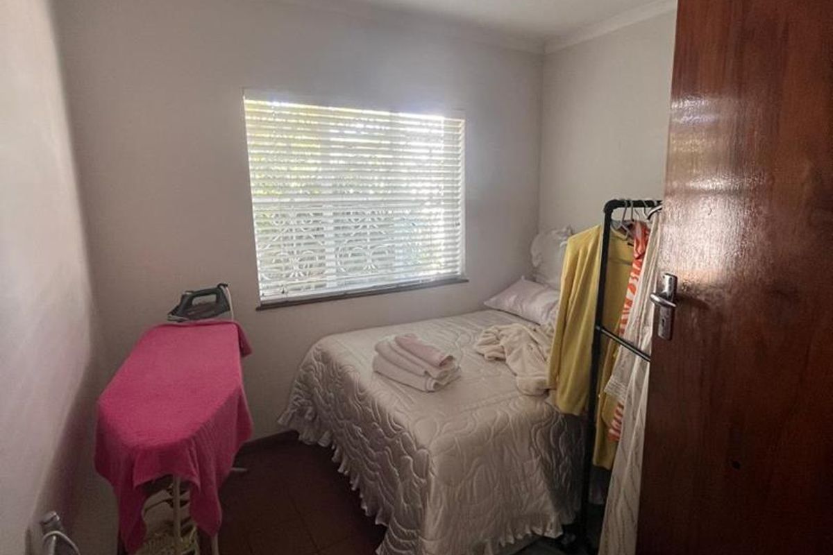 A compact bedroom featuring tiled flooring, a window with venetian blinds, and a solid wood door.