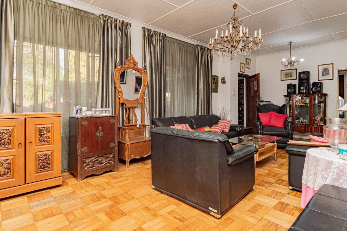 Spacious living room featuring classic parquet flooring, a decorative crystal chandelier, and coved ceiling details, offering a traditional and well-maintained living space.
