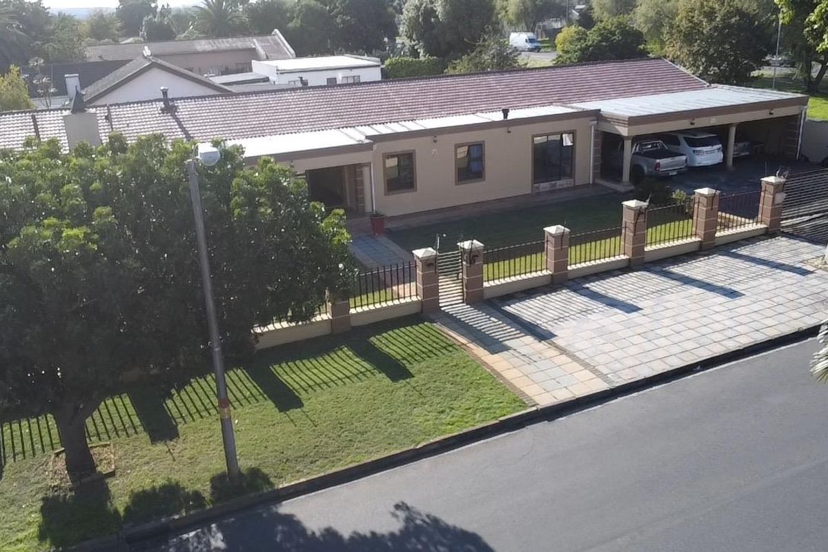 Aerial view of a single-story residential property featuring a tiled roof, paved driveway, front garden, and integrated carport.