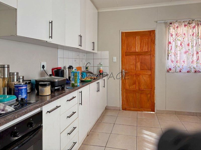 A functional kitchen featuring white cabinetry, laminate countertops, tiled backsplash, and a built-in oven, with direct access to an exterior wooden door.