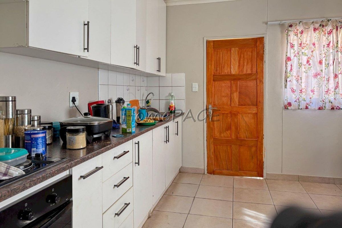 A functional kitchen featuring white cabinetry, laminate countertops, tiled backsplash, and a built-in oven, with direct access to an exterior wooden door.