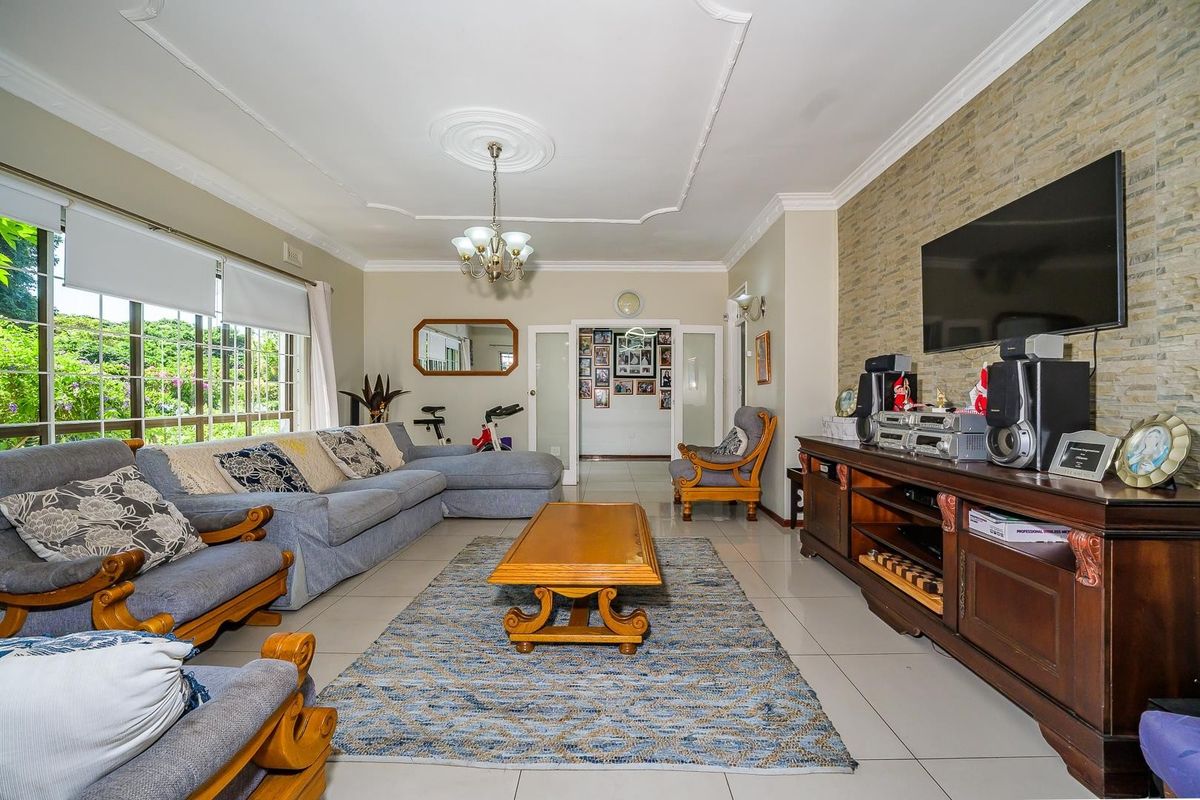 Spacious living room featuring a stone accent wall, decorative ceiling rose, and large windows providing natural light and garden views.