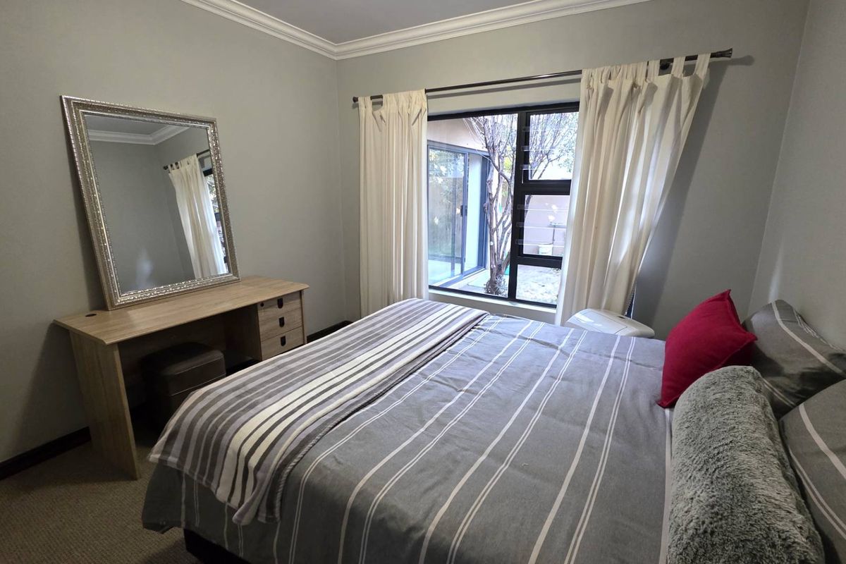 A well-maintained bedroom featuring neutral wall tones, carpeted flooring, and a large window providing natural light and garden views.