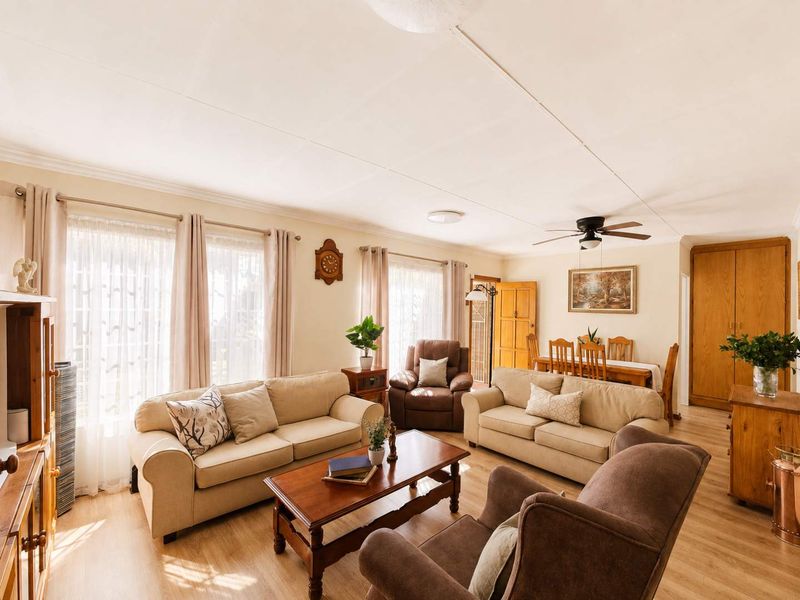 Spacious open-plan living and dining area featuring light laminate flooring, coved ceilings, a ceiling fan, and integrated storage cupboards.