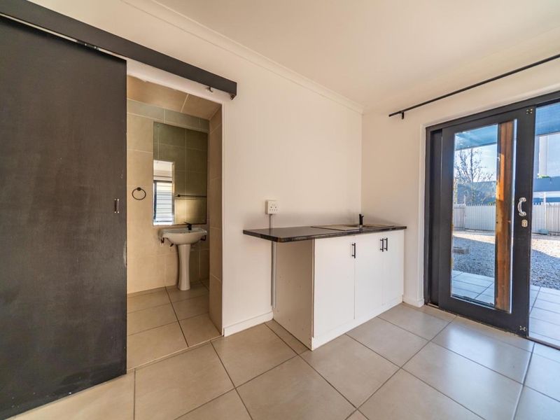 A functional utility space featuring tiled flooring, built-in cabinetry with a sink, and direct access to an outdoor area via a glass door.