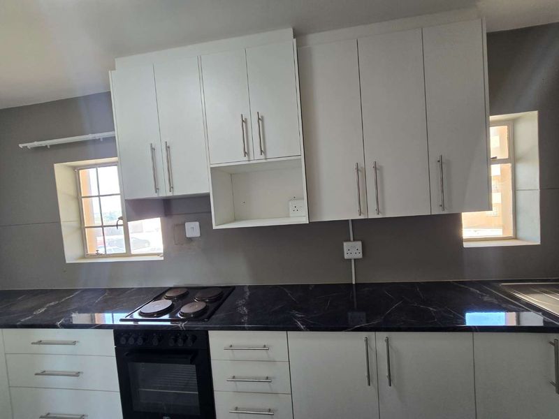 A functional kitchen featuring white cabinetry, black marble-effect countertops, a built-in oven, and an electric hob, ready for final finishing touches.