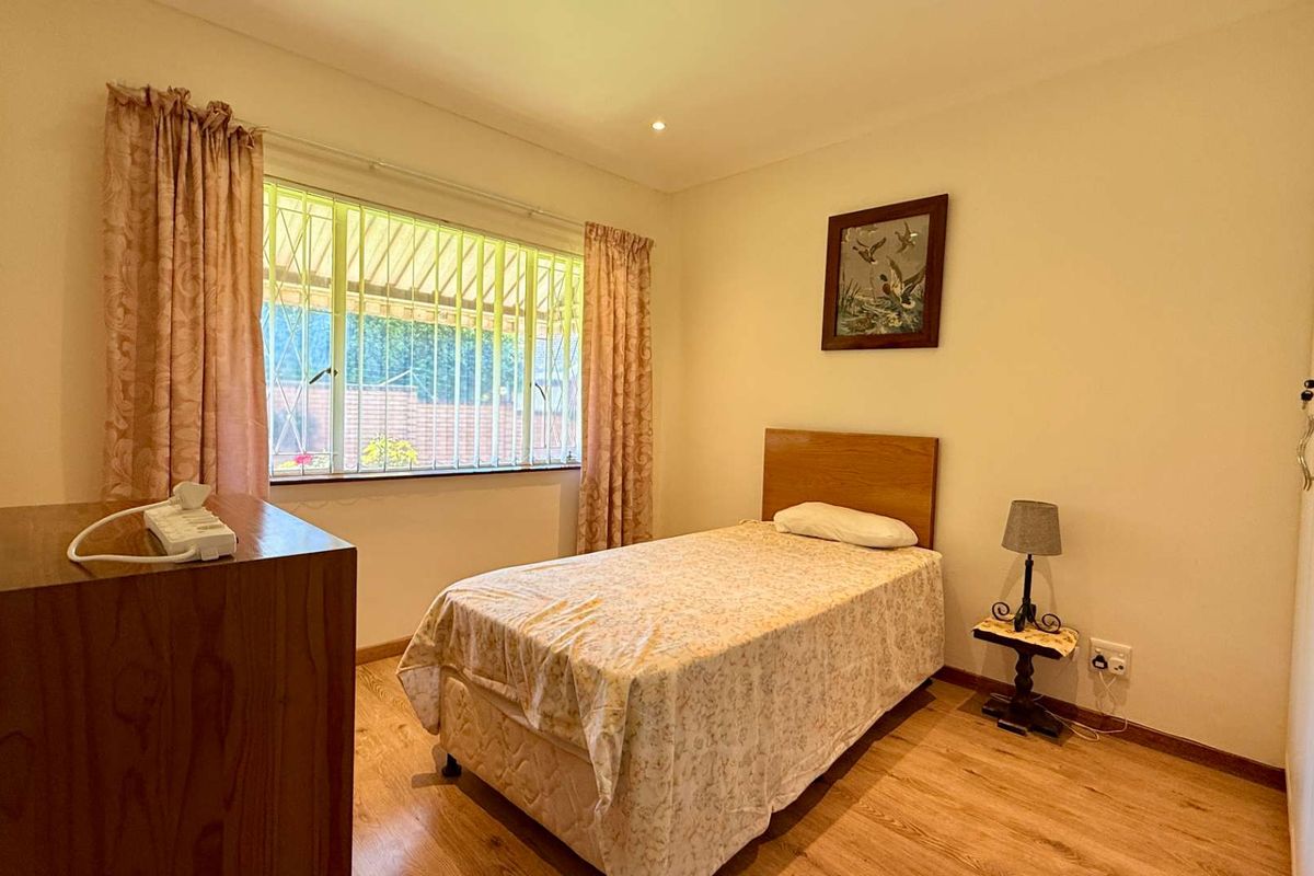 A functional bedroom featuring laminate flooring, built-in wardrobe storage, and a window fitted with security bars for added peace of mind.