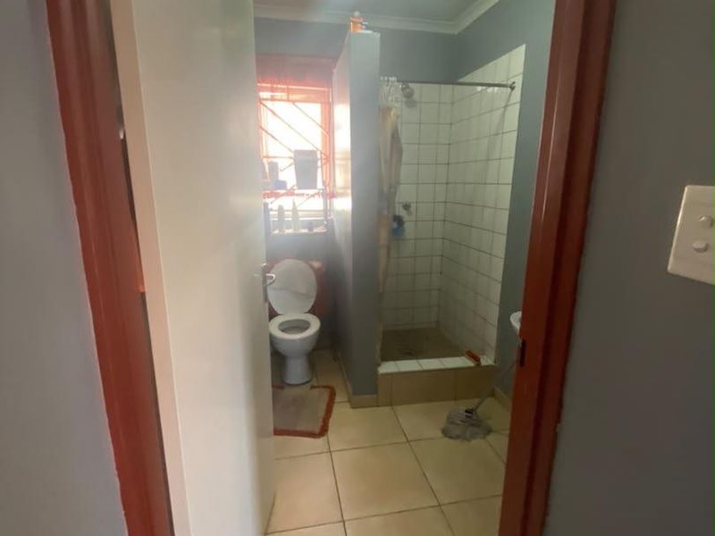 A functional bathroom featuring a shower enclosure, toilet, and tiled finishes, requiring cosmetic updates to modernize the space.