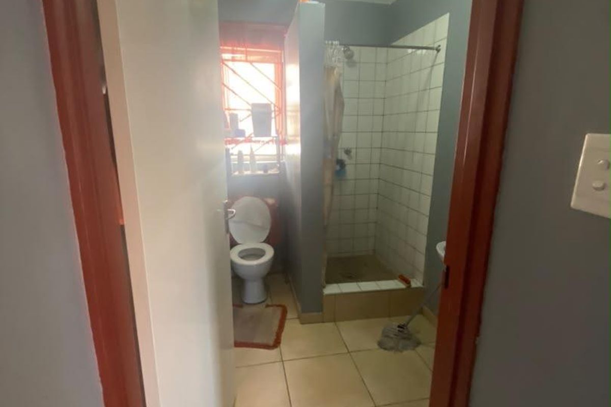 A functional bathroom featuring a shower enclosure, toilet, and tiled finishes, requiring cosmetic updates to modernize the space.