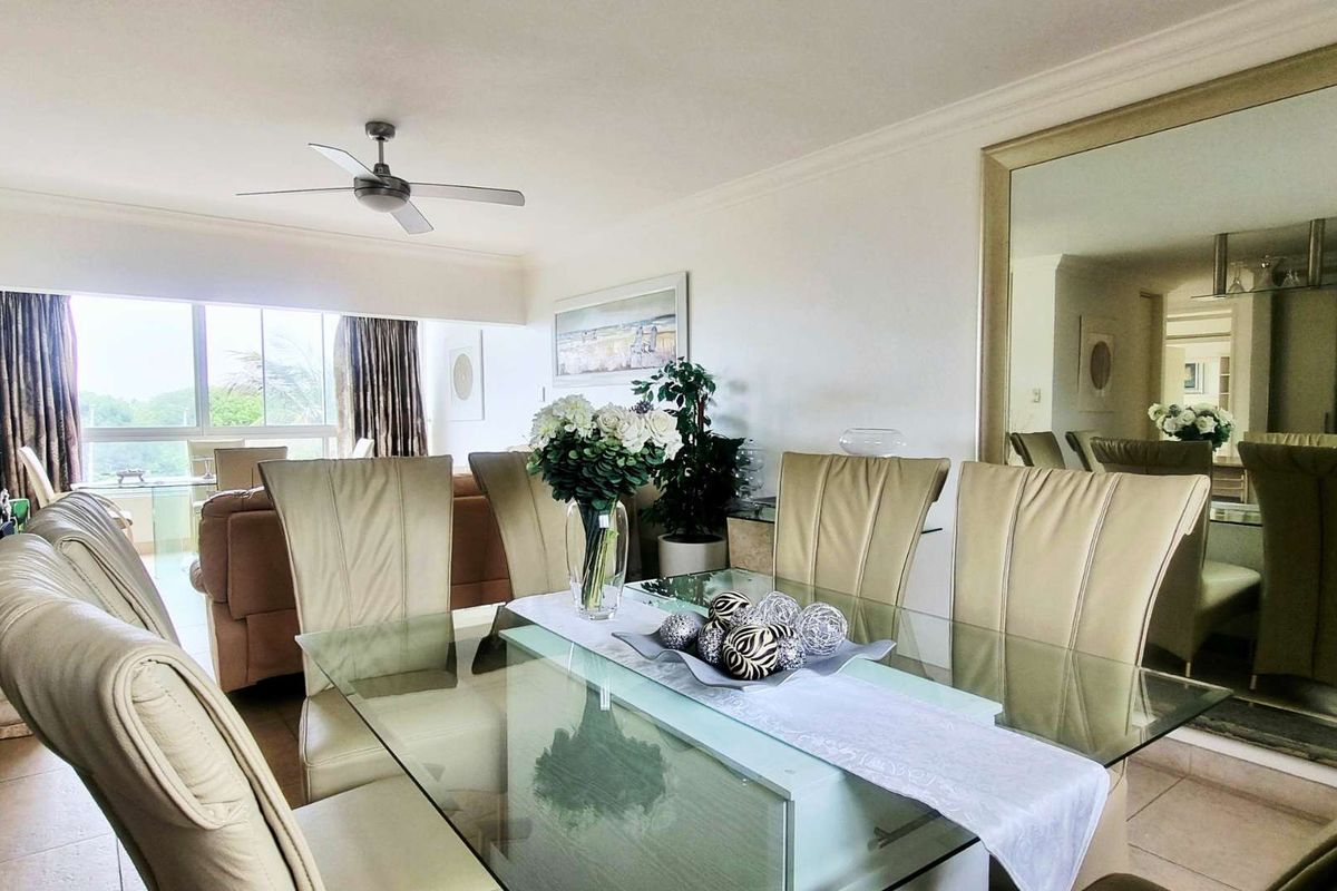 An open-plan living and dining area featuring tiled flooring, a ceiling fan, and a large wall mirror, with access to a balcony through sliding doors.