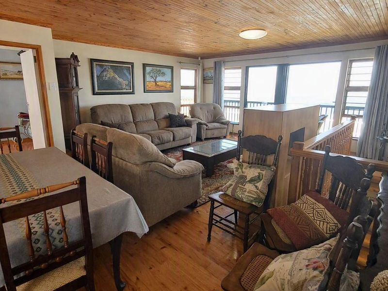 Open-plan living and dining area featuring warm timber ceilings and flooring, with direct access to a balcony through large windows.