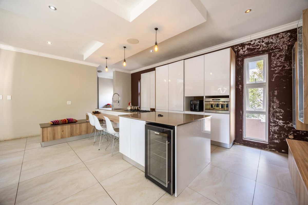 Modern kitchen featuring a central island with integrated wine cooler, built-in appliances, and sleek cabinetry, though the adjacent wall finish requires repair.