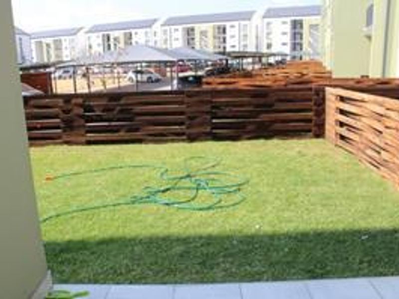 A private ground-floor garden area featuring a small lawn, tiled patio space, and wooden perimeter fencing within a residential apartment complex.