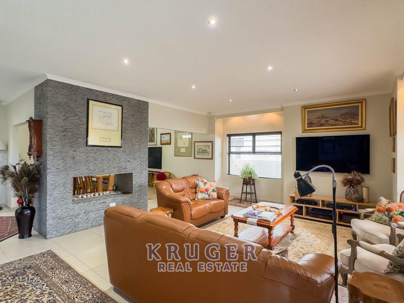 Spacious living room featuring a prominent stone-clad fireplace, neutral tiled flooring, and recessed downlighting, creating a comfortable and well-maintained family space.