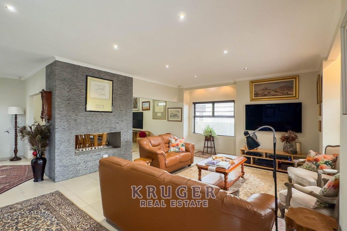 Spacious living room featuring a prominent stone-clad fireplace, neutral tiled flooring, and recessed downlighting, creating a comfortable and well-maintained family space.