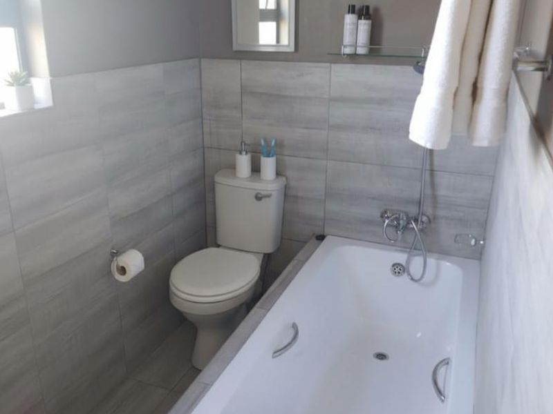 A clean, modern bathroom featuring neutral grey wall tiles, a standard bathtub with shower mixer, and a white toilet.
