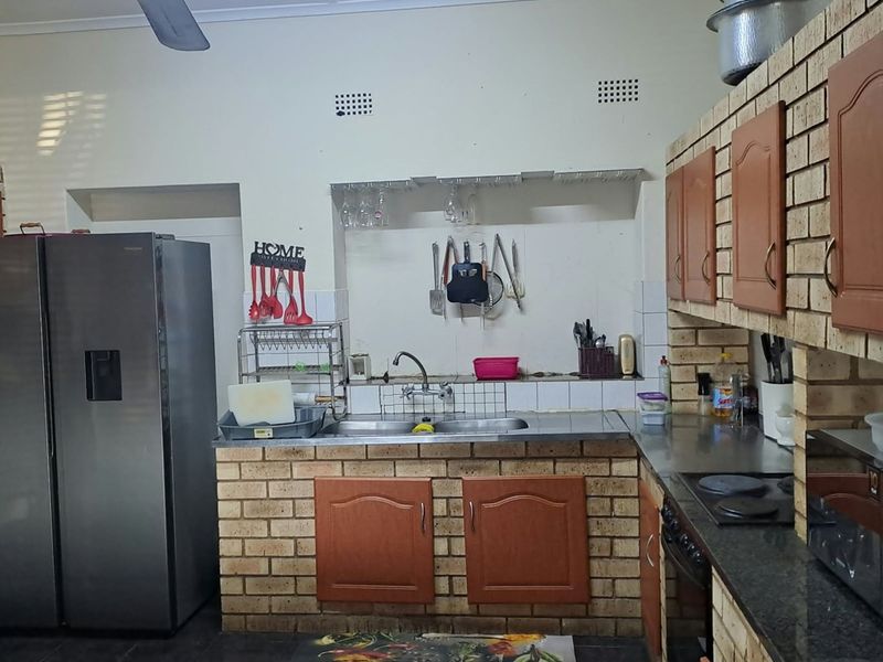 A functional kitchen featuring brick-built cabinetry, a double sink, built-in oven, and hob, with dark tiled flooring and a ceiling fan.