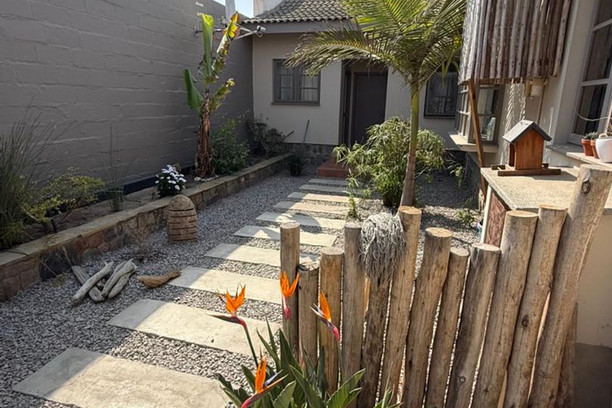 A well-maintained rear garden area featuring a stone-paved walkway, gravel landscaping, and a rustic timber pole fence.