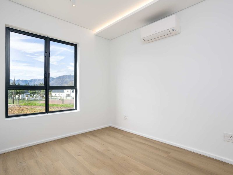 A bright, modern, and empty bedroom featuring light laminate flooring, a split-system air conditioner, and a large window with mountain views.