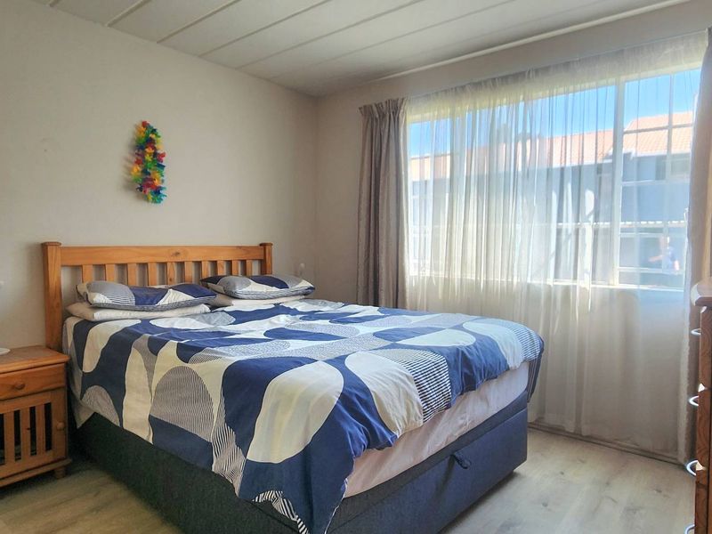 A functional bedroom featuring laminate flooring and a large window with curtain tracks, providing natural light.