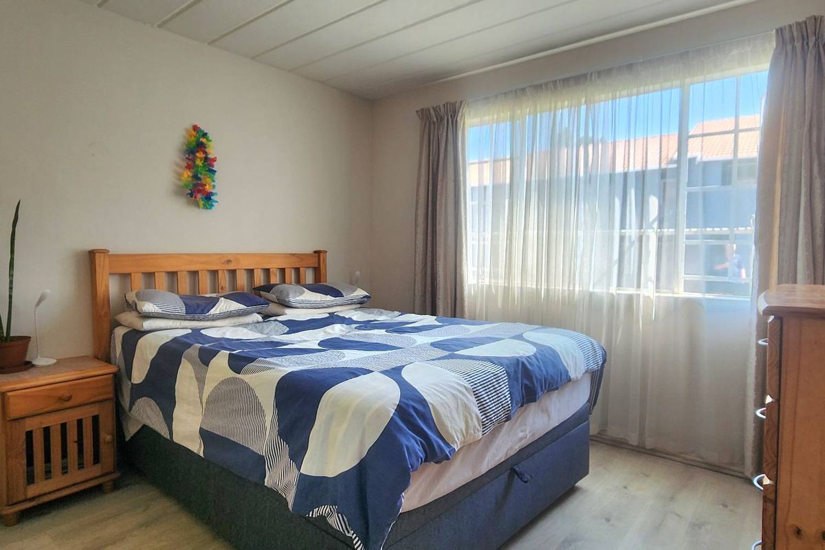A functional bedroom featuring laminate flooring and a large window with curtain tracks, providing natural light.
