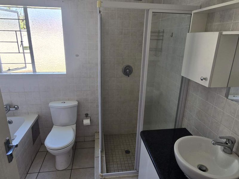 A functional bathroom featuring a shower enclosure, bathtub, vanity with basin, and tiled finishes throughout, offering a clean and practical layout.