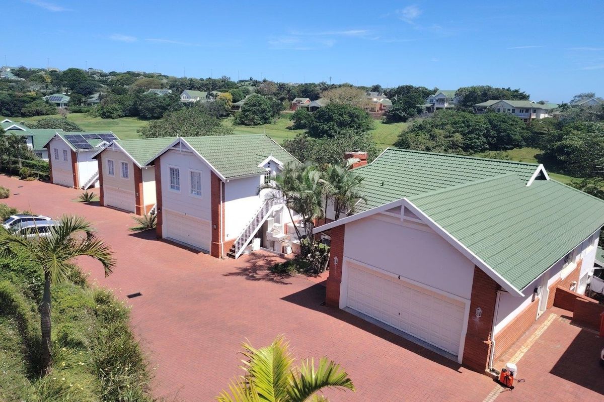 Aerial view of a townhouse complex featuring brick facades, green tiled roofs, paved driveways, and integrated garages within a landscaped estate setting.