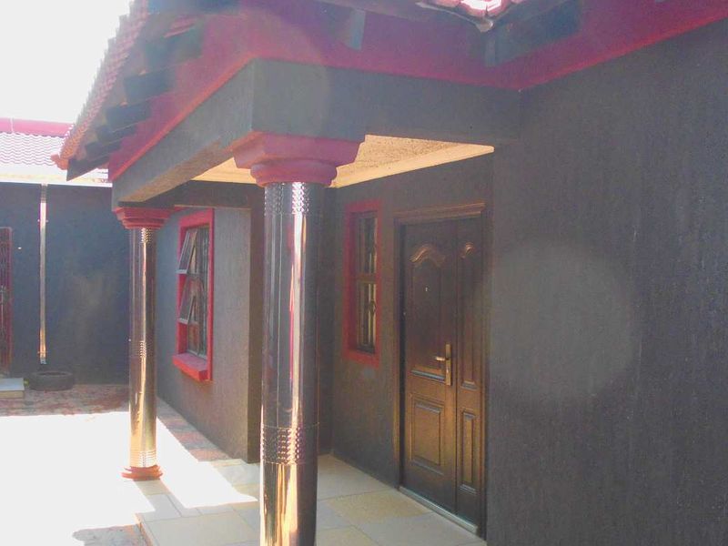 A covered patio area featuring tiled flooring, stainless steel support columns, and a tiled roof, providing a sheltered entrance to the home.