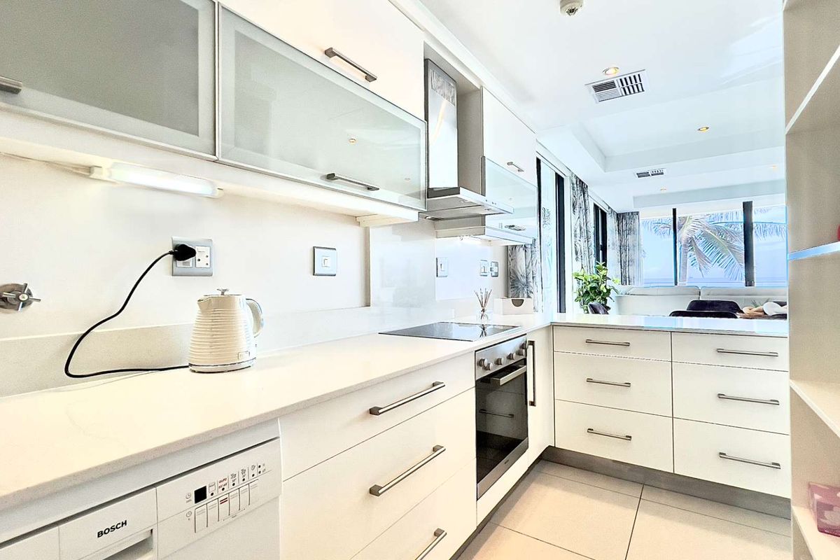 Modern kitchen featuring white cabinetry, stone countertops, integrated oven, hob, and extractor fan, with an open-plan layout leading to the living area.