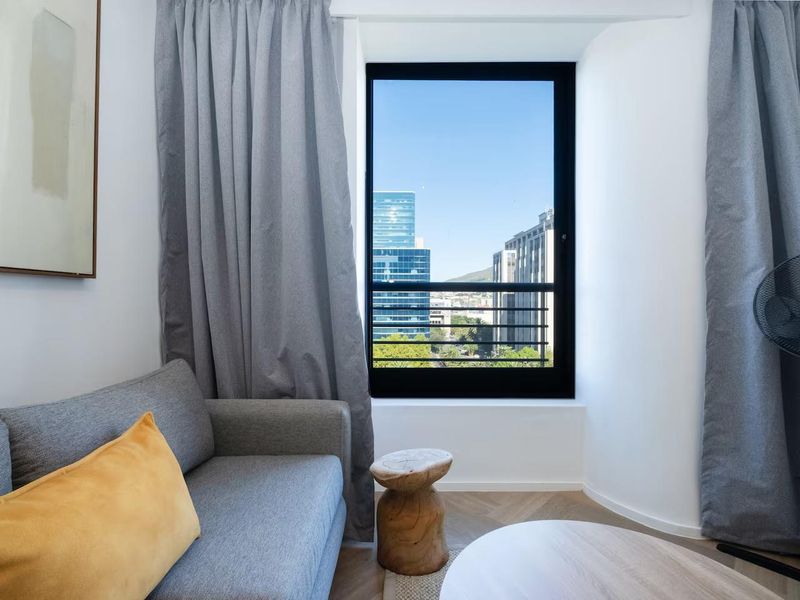 A bright living area featuring modern herringbone flooring and a large window with urban city views.