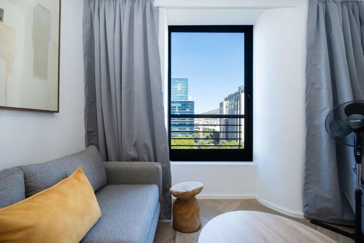 A bright living area featuring modern herringbone flooring and a large window with urban city views.