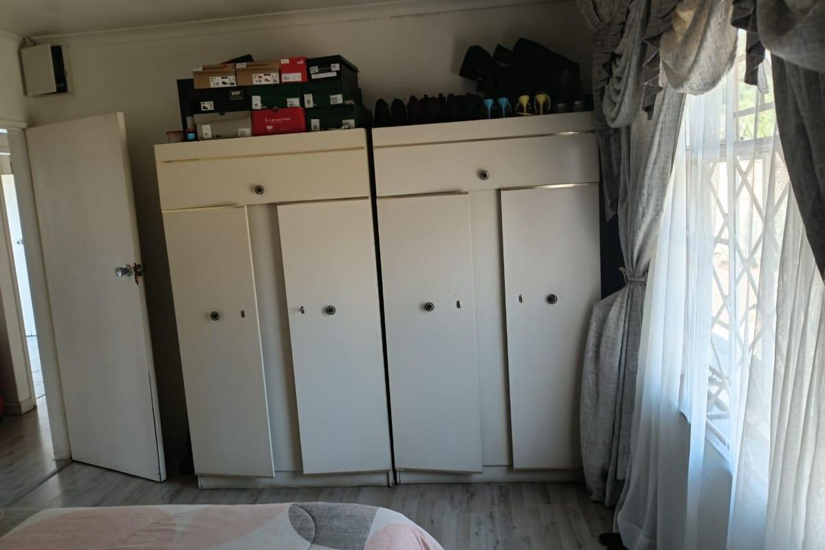 Bedroom featuring built-in cupboards with laminate flooring and a window fitted with a security gate.