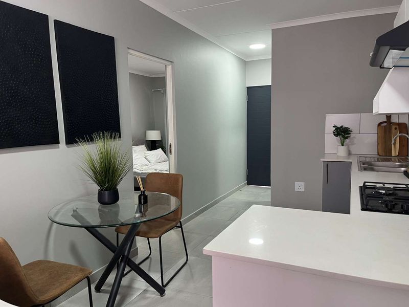Modern open-plan kitchen and dining area featuring sleek cabinetry, quartz countertops, gas hob, and contemporary tiled flooring with neutral wall finishes.