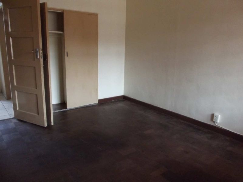An empty bedroom featuring dark parquet flooring, a built-in cupboard, and neutral walls, offering a blank canvas for renovation or staging.
