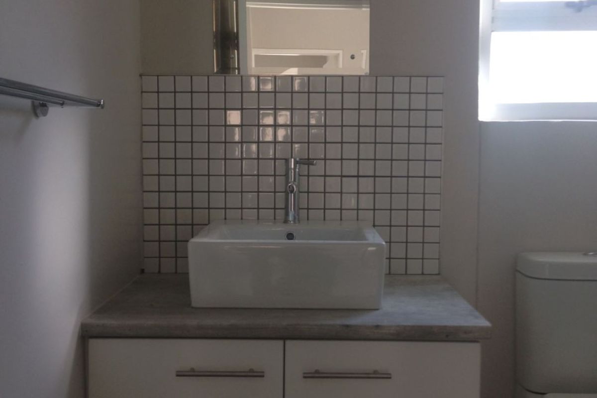 A modern bathroom featuring a wall-mounted vanity with a vessel sink, tiled splashback, and a wall-mounted mirror.