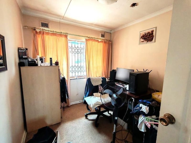 A compact bedroom featuring carpet flooring, a security gate on the window, and coving, currently utilized as a home office space.