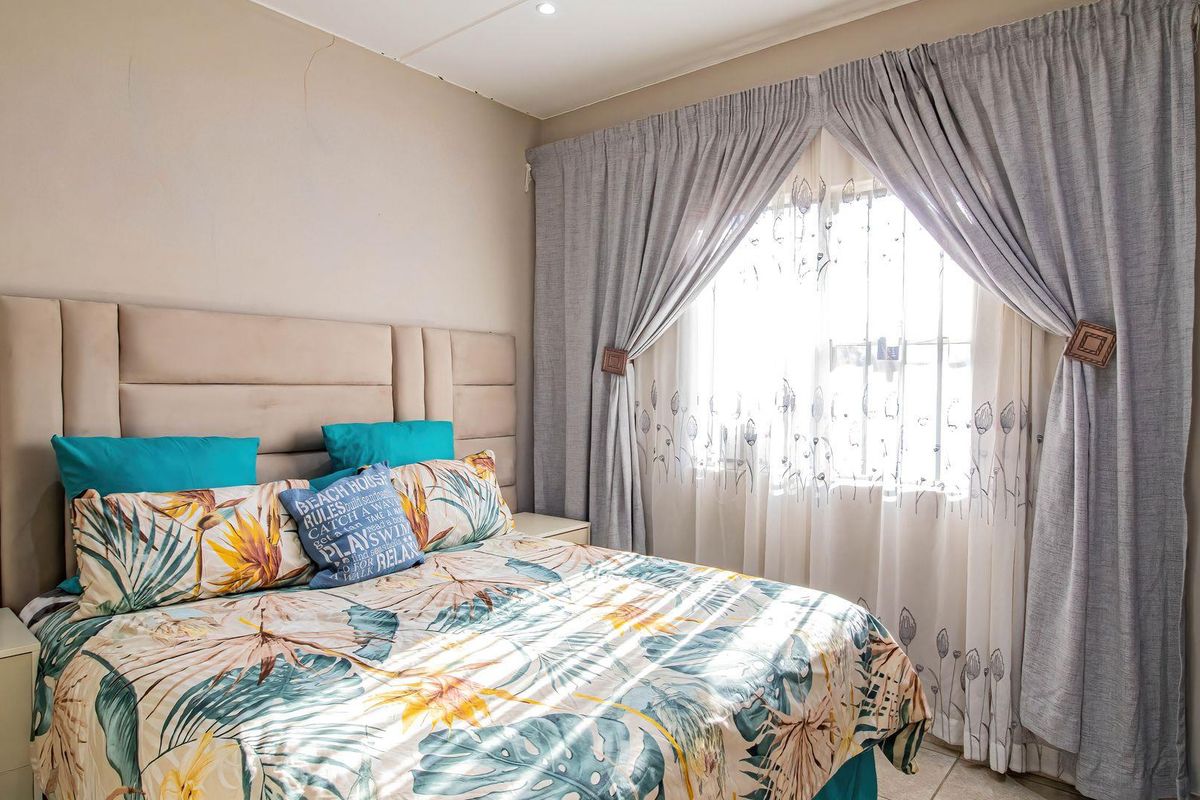 A cozy bedroom featuring a large upholstered headboard, built-in wardrobe storage, and natural light filtered through window curtains.