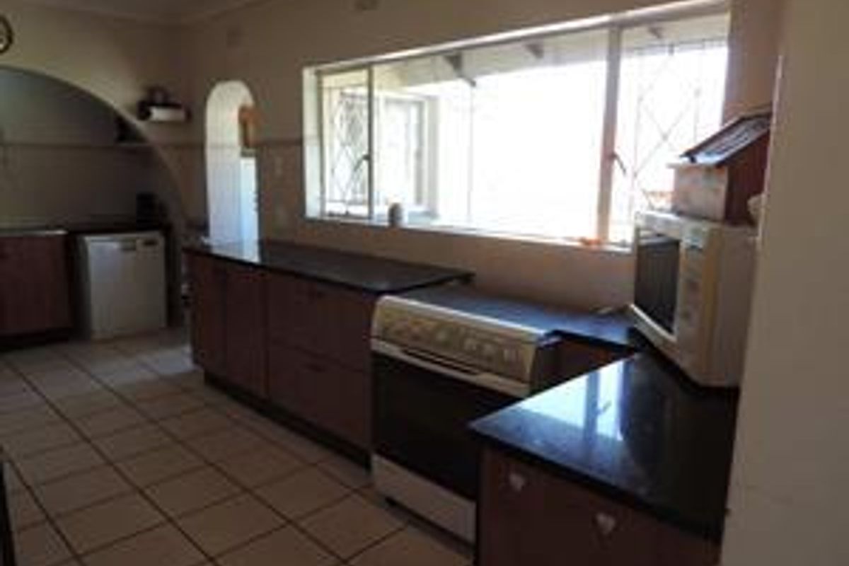 A functional kitchen featuring dark granite countertops, wooden cabinetry, tiled flooring, and a large window providing natural light.