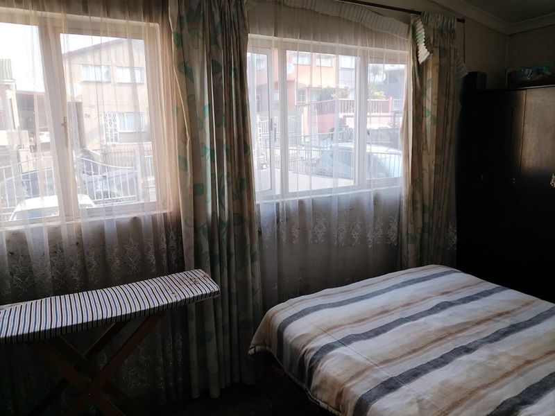 A bedroom featuring aluminium window frames and curtain rails, offering natural light and a view of the street.
